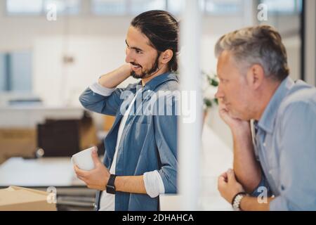 Lächelnder junger Geschäftsmann hält Kaffeetasse im neuen Büro Stockfoto