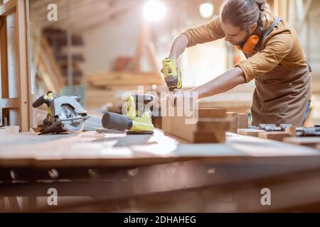 Zimmermann arbeitet mit modernen Akku-Werkzeugen und Holzstangen auf Die Werkbank in der Werkstatt Stockfoto