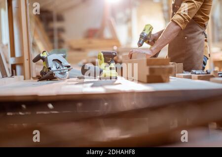 Zimmermann arbeitet mit modernen Akku-Werkzeugen und Holzstangen auf Die Werkbank in der Werkstatt Stockfoto