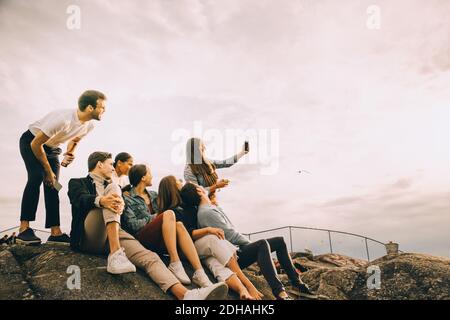 Frau, die Selfie mit Freunden auf Felsformation gegen Himmel Im Picknick Stockfoto