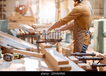 Zimmermann sägt Holzstäbe mit schnurloser elektrischer Säge am Tischlerwerkstatt Stockfoto