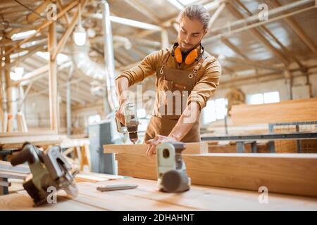 Zimmermann arbeitet mit modernen Akku-Werkzeugen und Holzstangen auf Die Werkbank in der Werkstatt Stockfoto