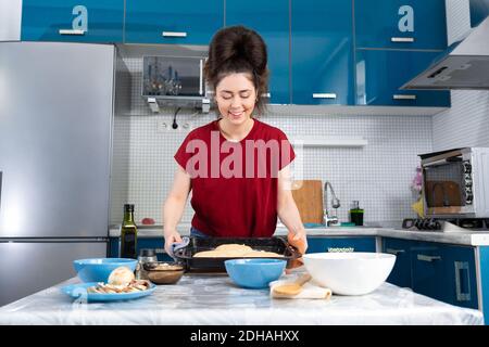 Eine schöne junge Frau hält ein Backblech mit Pizzateig. Das Konzept der Hausmannskost und Slow Food. Stockfoto