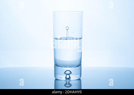 Wassertropfen spritzen in Glas halb voll vor hellem Hintergrund. Stockfoto