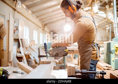 Zimmermann sägt Holzstäbe mit schnurloser elektrischer Säge am Tischlerwerkstatt Stockfoto