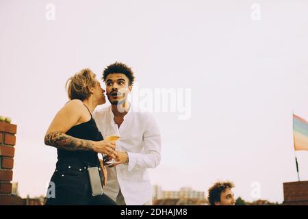 Frau, die etwas getrunken hat, während sie mit einem jungen Mann über Klatsch und Tratsch schalt Terrasse bei Dachparty Stockfoto