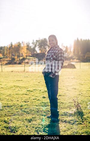 In voller Länge Porträt einer lächelnden Bäuerin, die Hände im Stehen hält Taschen auf dem Feld Stockfoto