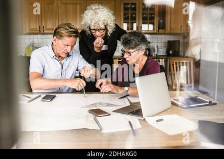 Weibliche Ausbilderin erklärt älteren Mann und Frau über Laptop bei Tabelle während des Navigationskurses Stockfoto