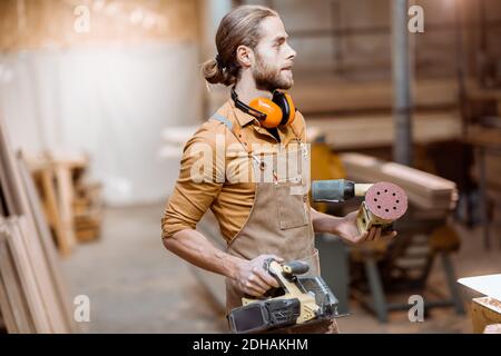 Porträt eines schönen Zimmermanns in Uniform mit modernen Werkzeugen In der Schreinerei Stockfoto