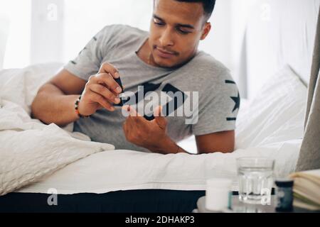 Mann, der zu Hause auf dem Bett liegt und einen medizinischen Test macht Stockfoto