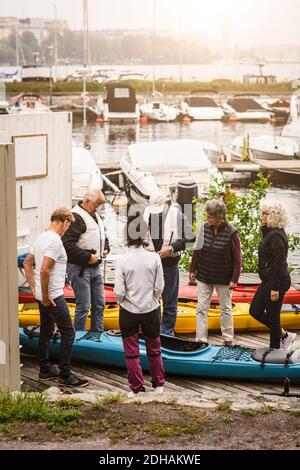 Ältere Männer und Frauen, die den männlichen Lehrer im Leben betrachten Jacke im Stehen bei Kajaks Stockfoto