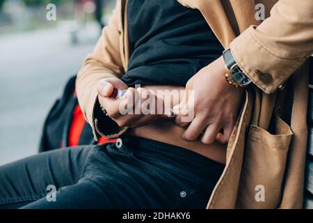 Mittelteil des Mannes, der Insulin injiziert, während er auf der Bank sitzt Stockfoto