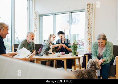 Pensionierte ältere Frau lehrt Stricken männlichen Krankenschwester während sitzen Inmitten von Freunden im Altenheim Stockfoto