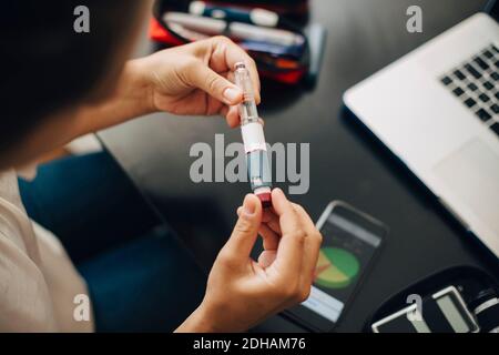 Zugeschnittenes Bild einer Geschäftsfrau, die den Injektionsstift hält, während sie sitzt Schreibtisch Stockfoto