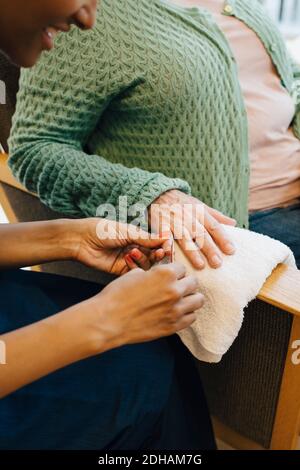 Mittelteil der älteren Frau bekommen ihre Nägel in Form von Junge weibliche Hausmeisterin im Pflegeheim Stockfoto