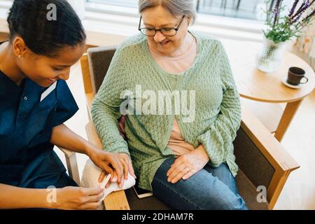 Lächelnde ältere Frau, die junge Hausmeisterin ansieht, die sie einreicht Nägel in Altersheim Stockfoto