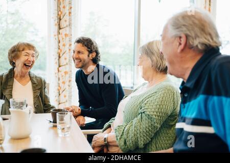 Lächelnder Mann, der seine Großmutter und ihre Freunde im Ruhestand besucht Zu Hause Stockfoto