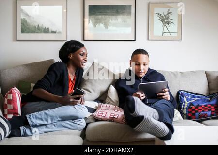 Die ganze Länge der Mutter betrachtet Sohn mit digitalen Tablet Auf dem Sofa zu Hause Stockfoto