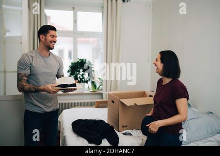 Glücklicher Mann mit Hut im Gespräch mit Frau Klamotten durch Bett zu Hause Stockfoto