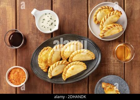 Empanadas mit Saucen und Wein, von oben auf einem rustikalen Holzhintergrund geschossen Stockfoto