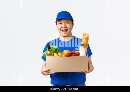 Online-Shopping, Lebensmittelzustellung und Versandkonzept. Fröhlich lächelnd junger asiatischer Kurier in blauer Uniformhandbox mit groce Stockfoto