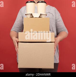Frau in grauer Kleidung hält einen Stapel braunes Papier Boxen und Einweg-Gläser mit Kaffee auf einem roten Stockfoto