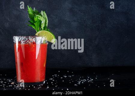 Bloody Mary Cocktail in einem hohen Glas, serviert mit Limette und Sellerie, Seitenansicht auf dunklem Hintergrund Stockfoto