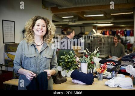 Porträt einer lächelnden reifen Frau, die gegen Kollegen steht, die in arbeiten Lager Stockfoto