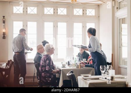 Die Besitzer servieren Kaffee für männliche und weibliche Freunde, die an ihnen sitzen Restauranttisch Stockfoto