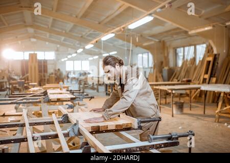 Schöner Zimmermann in gleichmäßigen verleimenden Holzstäben mit Handdruck Bei der Zimmermannsherstellung Stockfoto