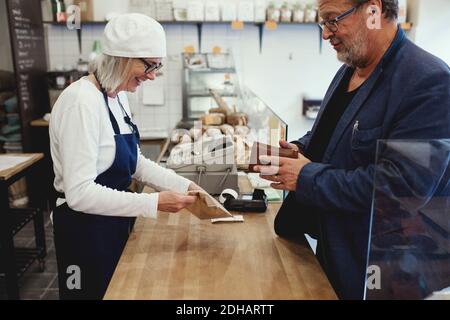 Männliche Kunden zahlen weibliche Bäcker, während an der Kasse Ecke stehen In der Bäckerei Stockfoto