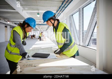 Seitenansicht von Ingenieurinnen, die bei der Konstruktion über Baupläne diskutieren Standort Stockfoto