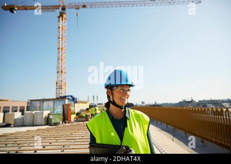 Lächelnde Ingenieurin in reflektierender Kleidung mit digitalem Tablet Baustelle gegen klaren Himmel Stockfoto