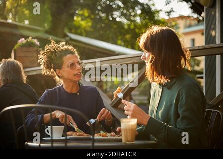 Weibliche Architekten diskutieren beim Mittagessen im Café im Freien während Sonniger Tag Stockfoto