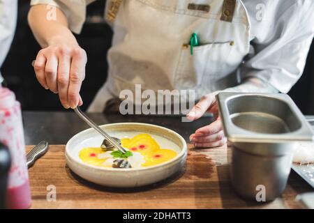 Mittelteil der weiblichen Köchin garnieren Essen mit Kraut in Teller An der Theke in der Küche Stockfoto