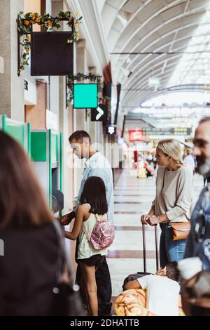 Mann mit Familie kauft Fahrkarten von Automat im Zug Station Stockfoto