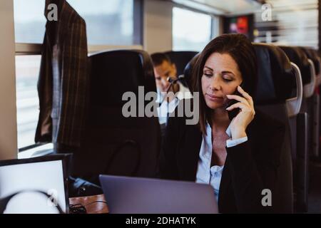 Geschäftsfrau im Gespräch auf Smartphone und mit Laptop während der Fahrt Im Zug Stockfoto