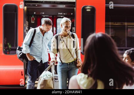 Glückliche Familie mit Gepäck, das am Bahnsteig gegen den Zug stand Stockfoto