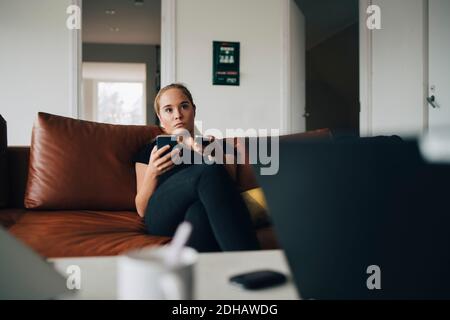 Teenager-Mädchen auf dem Sofa mit Smartphone und Fernbedienung sitzen Steuerung während Sie zu Hause Fernsehen Stockfoto