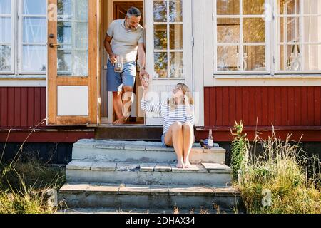 Männlicher Partner, der Frau im Stehen ein Glas Wasser gibt In der Tür an der Blockhütte Stockfoto