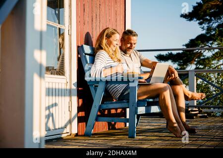 Lächelndes Paar mit Laptop beim Frühstück auf der Veranda Blockhütte Stockfoto