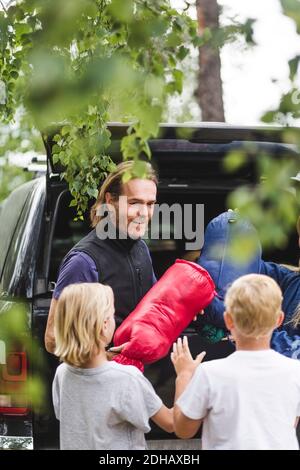 Lächelnder Vater, der Kindern Gepäck gab, während er aus dem Auto ausladende Stockfoto