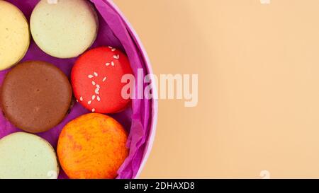 Bunte französische Macarons in rosa Pappkarton auf pfirsichfarbenem Hintergrund. Draufsicht. Stockfoto