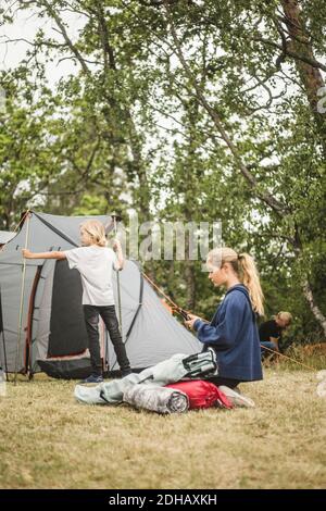 Teenager-Mädchen mit Telefon, während Familie Pitching Zelt auf Camping Standort Stockfoto