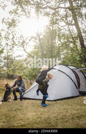 Mann, der mit Hund sitzt, während die Kinder beim Zelten spielen Stockfoto