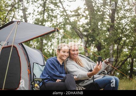 Glückliche Mutter nimmt Selfie mit Tochter auf Smartphone während Zeltcamping Stockfoto