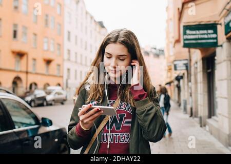 Lächelndes Mädchen, das Musik über das Smartphone hört, während es weiter geht Bürgersteig in der Stadt Stockfoto