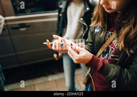 Mittelteil des Mädchens, das während des Gehens Kabel mit dem Mobiltelefon verbindet Mit Freunden Stockfoto