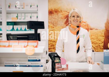 Porträt einer selbstbewussten Apothekerin, die an der Kasse gegen das Plakat steht Im medizinischen Geschäft Stockfoto