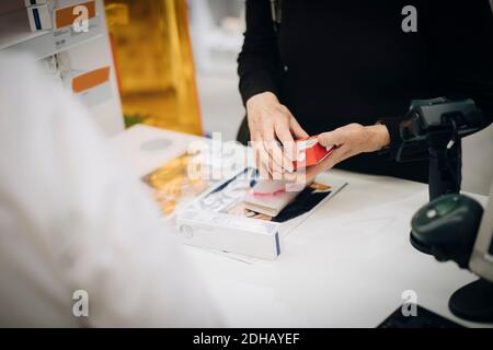 Mittelteil des Senior-Kunden hält verschreibungspflichtige Medizin mit weiblichen Besitzer An der Kasse in Apotheke Stockfoto